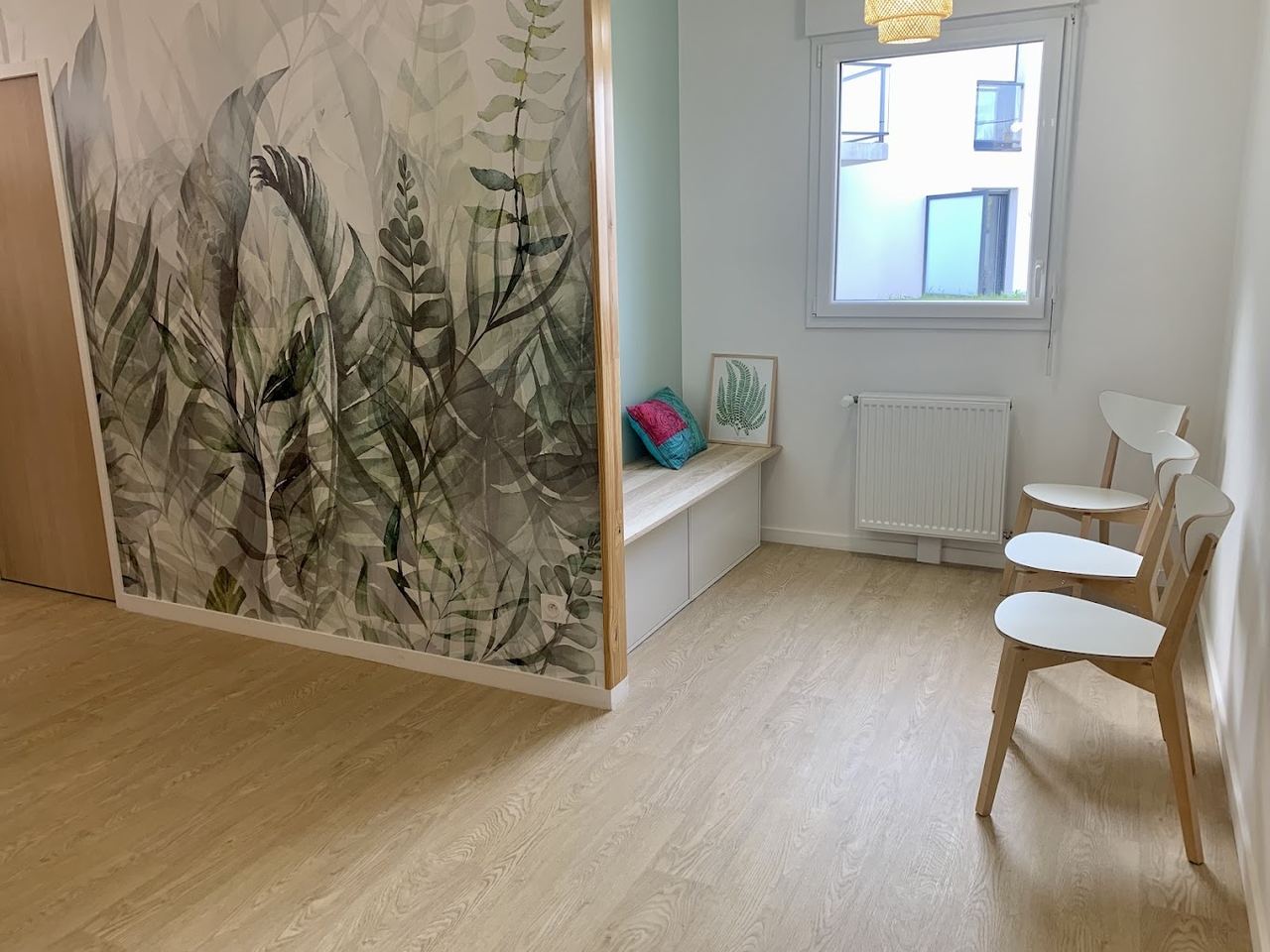 La salle d'attente du cabinet : fresque végétale à l'aquarelle, banc en bois clair, chaises blanches et grande fenêtre